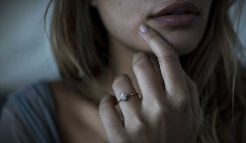A close-up of a person touching their face, showing a ring with a single stone on their finger.